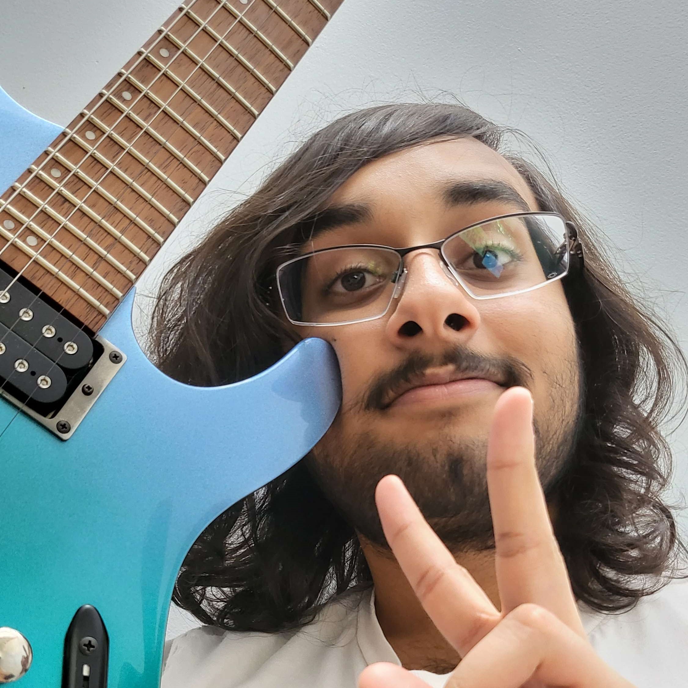 A selfie of me putting up a peace sign (two fingers), leaning on my blue electric guitar.